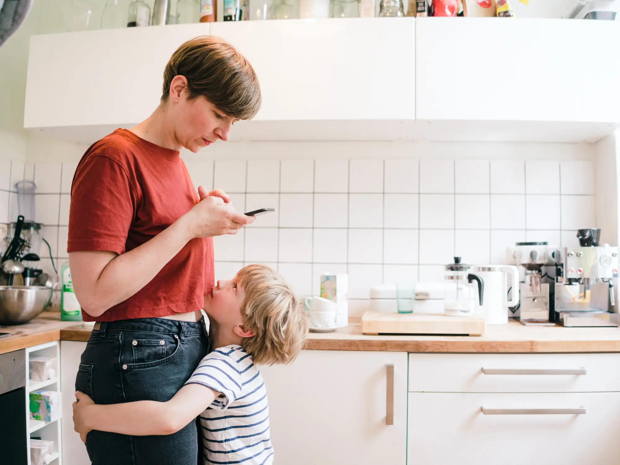 a woman looks at her phone while a kid looks up at her